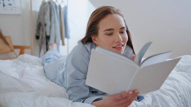 Женщина вблизи, глядящая на книгу, лежащая в удобной домашней постели, студент, поглощенный романом.