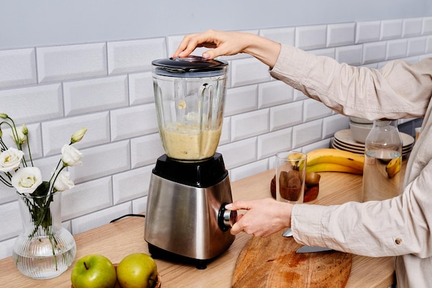 closeup of woman making fresh juice from fruits in blender standing in kitchen