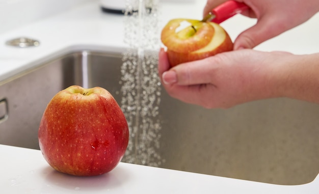 Foto primo piano della mela della sbucciatura della donna sopra il lavandino in cucina