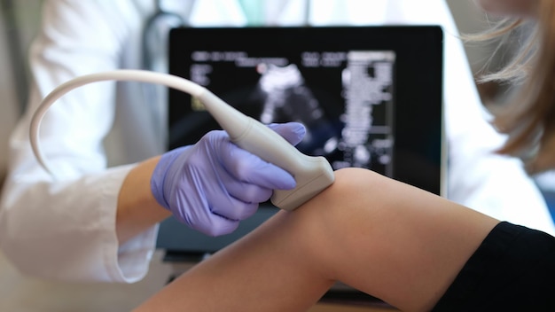 Closeup of woman physician diagnosing injuries or defects of kid ultrasound diagnostics of knee