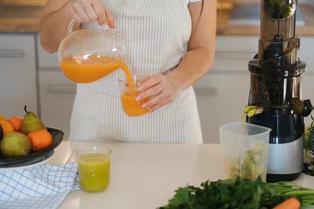 オレンジの自家製ジュースをガラスの中に注ぐ女性のクローズアップ キッチンのフルーツと