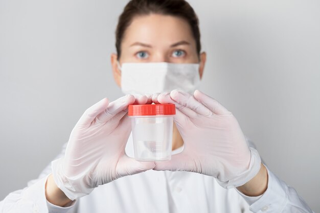 Closeup of a woman in a protective face mask with a container for analyzes