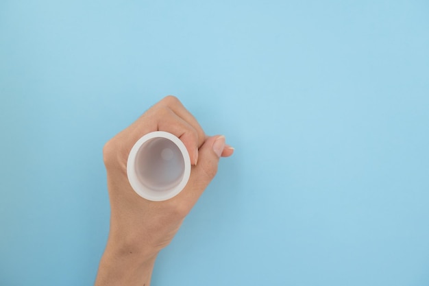 Closeup of a woman's hand holding a menstrual cup against a blue background Women's health