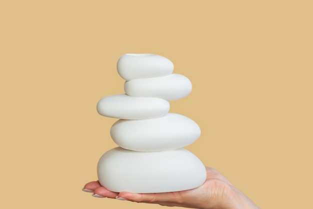 closeup of a woman's hand holding a pyramid of white oval stones holding the balance