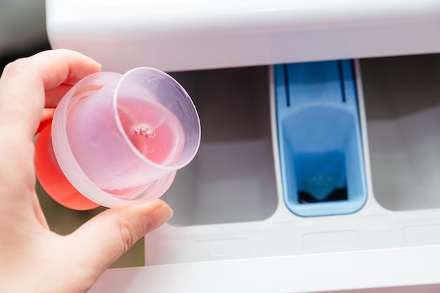 Closeup of a woman's hand pouring laundry detergent into a washing machine