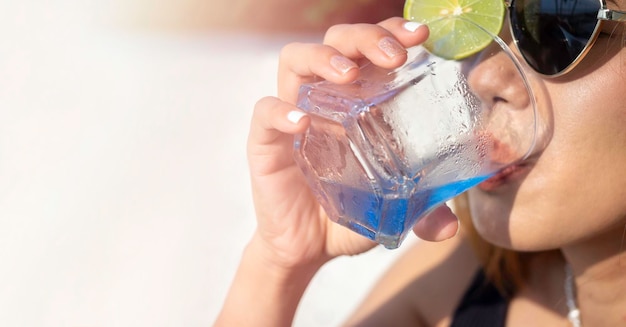 Крупным планом женская рука с блестящим модным лаком для ногтей держит синий коктейльный напиток с лаймом в коротком стакане приветственный напиток с копией пространства Летний фон баннера Женщина в солнцезащитных очках