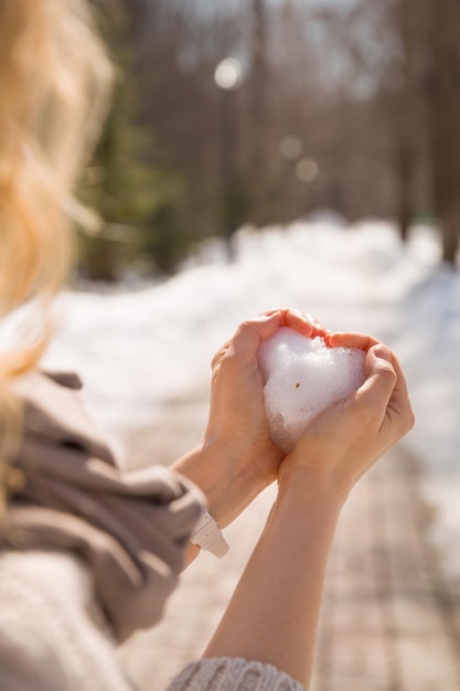 Closeup of woman's hands making heart out of snow Enjoying winter walking in the park on a sunny day