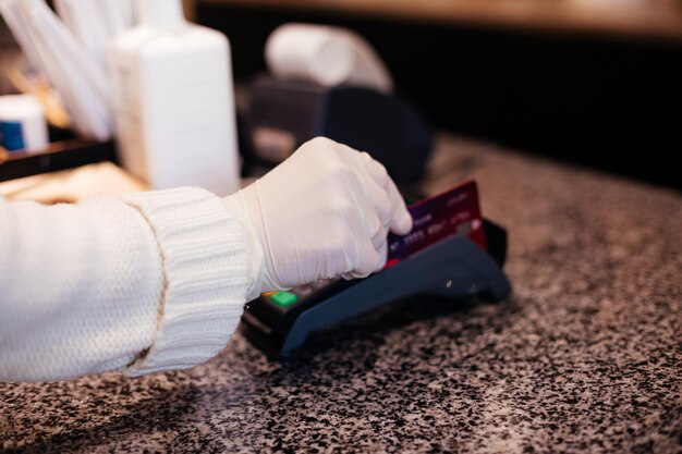 Foto le mani della donna del primo piano in guanti protettivi pagano al negozio usando la carta di credito per prevenire la diffusione del coronavirus la donna sceglie di pagare senza contanti tecnologie per servire la sicurezza