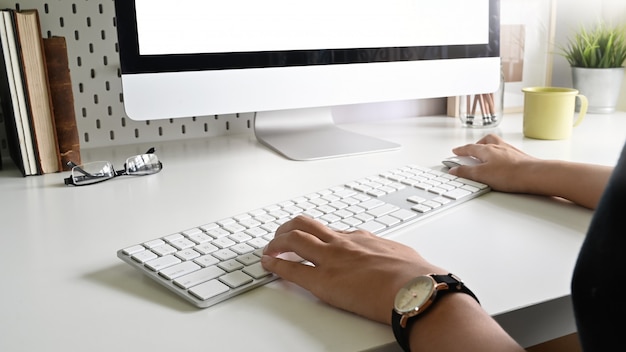 Le mani della donna del primo piano che scrivono la tastiera di computer a macchina sulla scrivania.