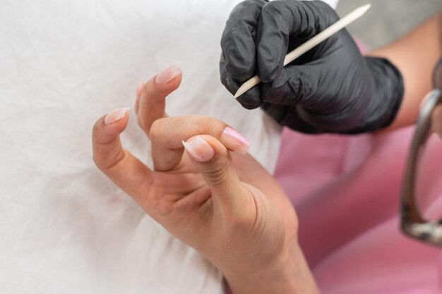 Foto primo piano delle mani di una donna usando un bastone di legno per rimuovere le imperfezioni della manicure