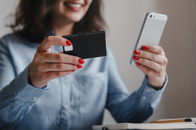 Closeup of woman's hands with red nails holding credit card and mobile phone making payment online