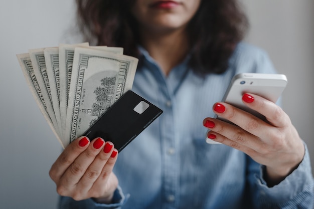 Closeup of woman's hands with red nails holding hundred dollars money banknotes, credit card and phone