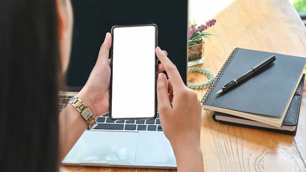 Closeup woman's holding smartphone with empty screen on office desk.