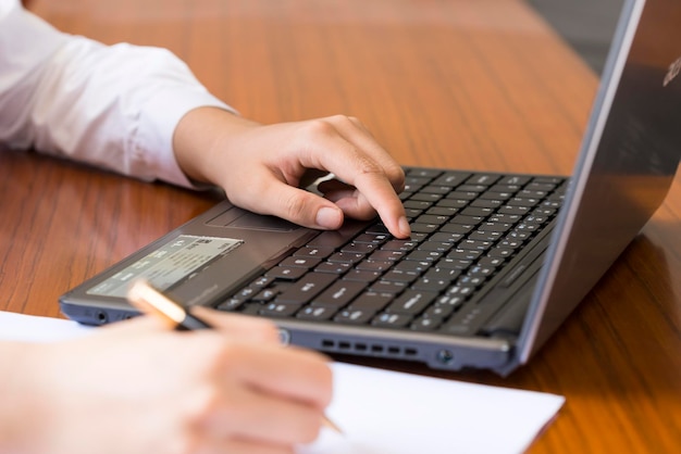 Primo piano una donna con una penna per camicia in mano che lavora su un laptop e prende appunti