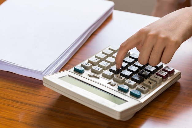 Closeup a woman in a shirt uses a calculator at her desk