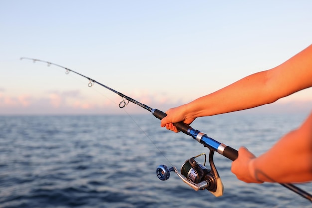 Closeup of woman sitting holding fish rod in hands female taking fish in sea or river fish and