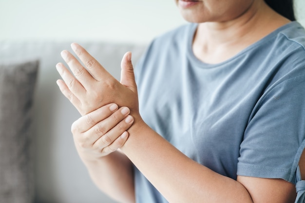 Closeup of woman sitting on sofa holds her wrist. hand injury,\
feeling pain. health care and medical concept.