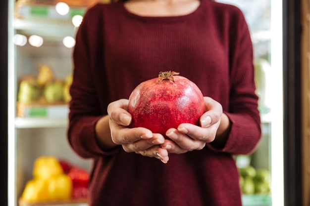 Closeup of woman standing and holding pomegranate at grocery store