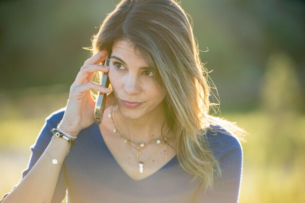 Foto close-up di una donna che parla al cellulare all'aperto in natura in una giornata di sole