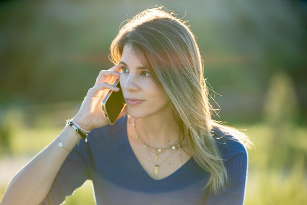 Foto close-up di una donna che parla al telefono mentre si rilassa all'aperto nella natura tecnologia e