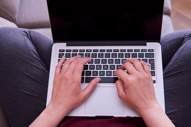 Closeup of a woman using a laptop on her legs