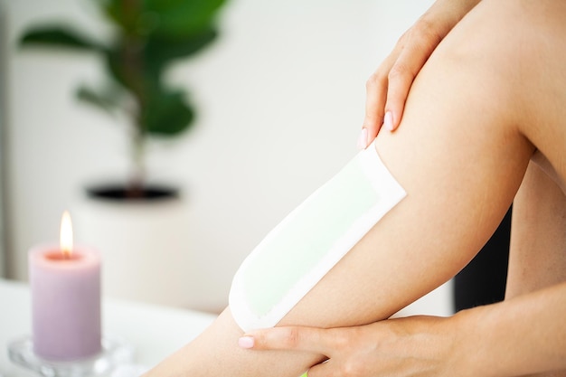 Closeup of woman waxing her leg at home bathroom