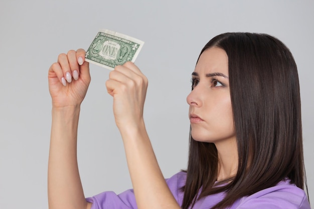 엄중 한 얼굴 을 가진 여자 가 손 에 달러 지폐 를 들고 진정성 을 확인 하고 있다