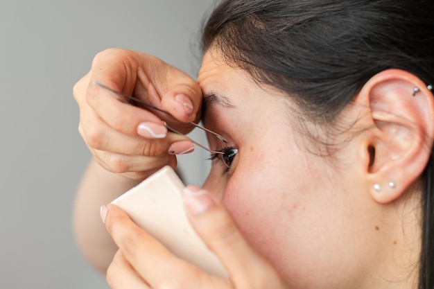 Closeup of a woman with tweezers arranging her false eyelashes with great care