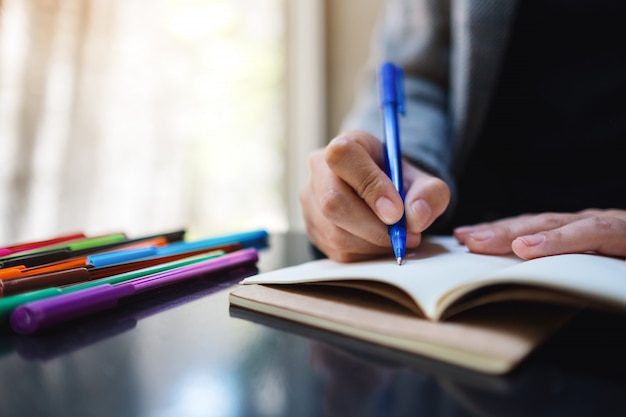 Closeup  of a woman writing on a blank notebook with colored pens on the table