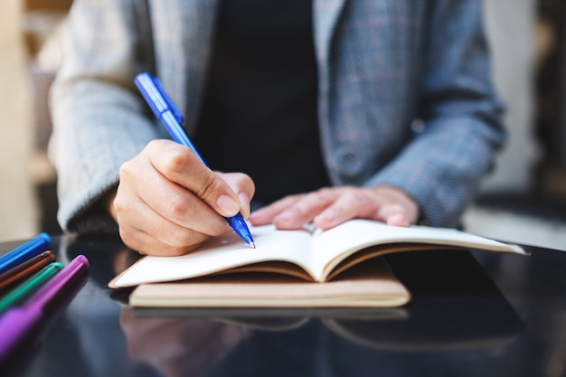 Closeup  of a woman writing on a blank notebook with colored pens on the table