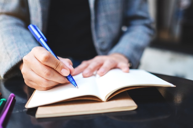 Closeup  of a woman writing on a blank notebook with colored pens on the table