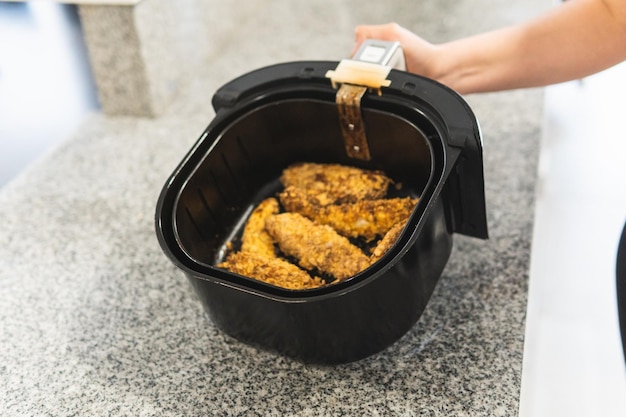 Closeup of woman39s hand using an air fryer with fried chicken in cereal batter