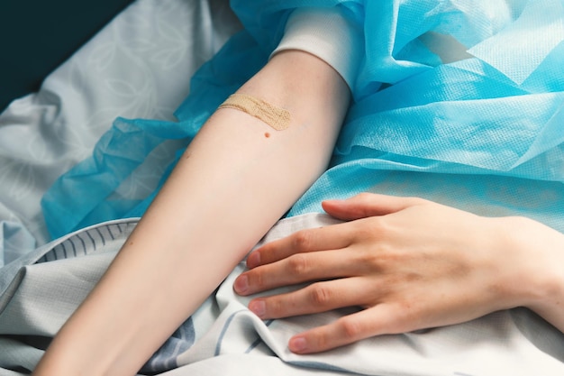 Closeup of a woman39s hand with a bandaid on her arm Patient lying on a hospital bed after surgery