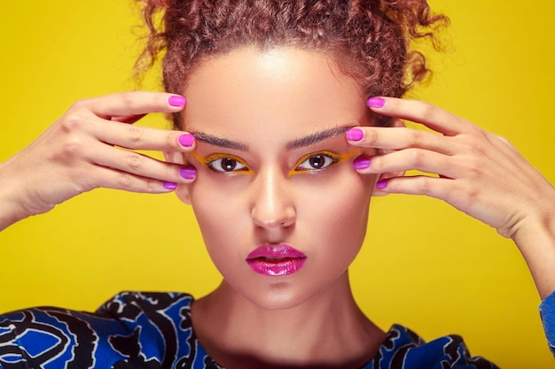 Closeup of a womans face with vibrant yellow and violet makeup against an english background