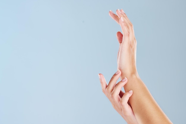 Крупный план женских рук с синим студийным фоном и копирайтом Увеличьте ухоженные ногти, касающиеся мягкой кожи после использования косметических процедур или маски для кожи Модель руки с копировальным пространством