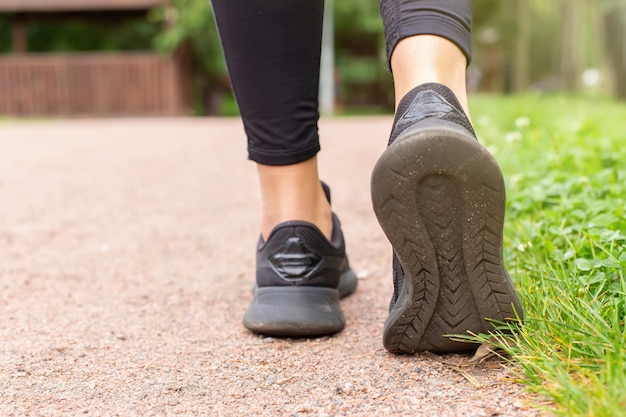 Closeup of a womans legs in black sneakers walking along a path made of small red stone