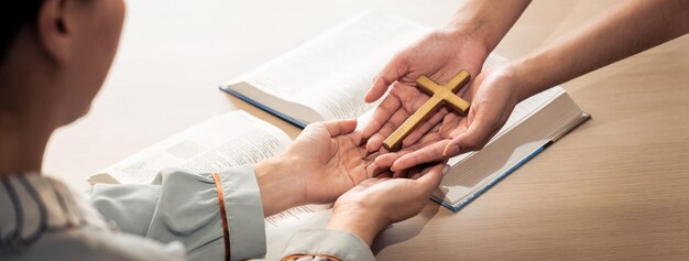 Closeup women prayer deliver holy bible book and holy cross to young believer Spreading religion symbol Concept of hope religion christianity and god blessing Warm background Burgeoning