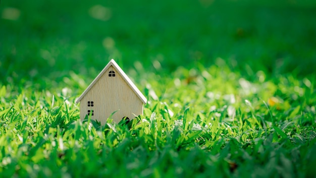 Casa di modello di legno del primo piano sulla priorità bassa dell'erba di luce solare