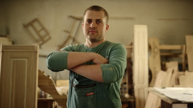 Closeup wood worker crossing arms in carpentry workshop Portrait of handsome carpenter laughing in studio Cheerful man looking at camera indoors Master posing in studio