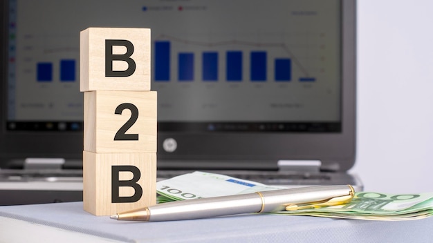 Photo closeup of wooden blocks with the word b2b and banknotes on the background of a laptop