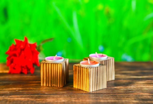 Closeup of wooden candle holders with tea light on red rose petals and blurred green background