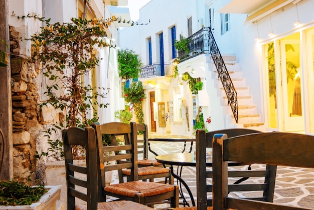 Closeup of wooden chairs and table on the background of white architecture with green trees