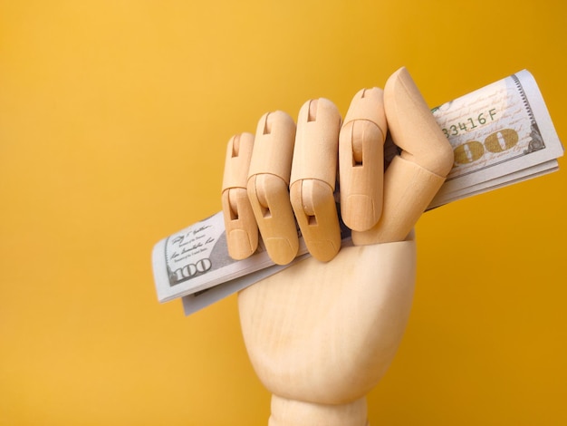 Closeup wooden hand grip banknotes on a yellow background