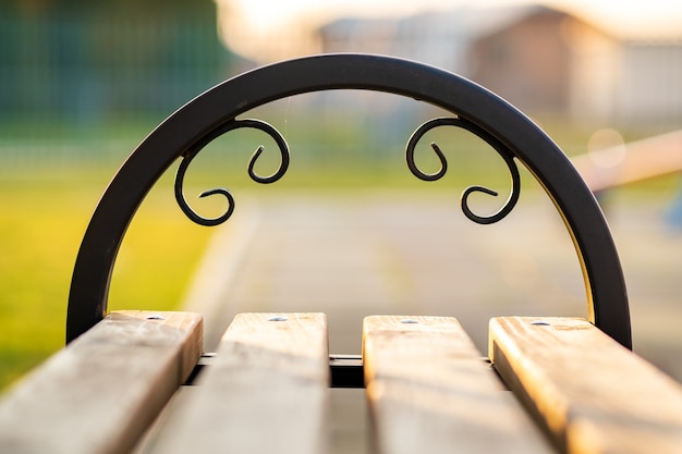 Closeup of wooden park bench with metal handgrip outdoors.