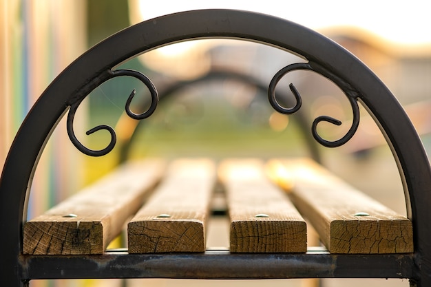 Closeup of wooden park bench with metal handgrip outdoors.