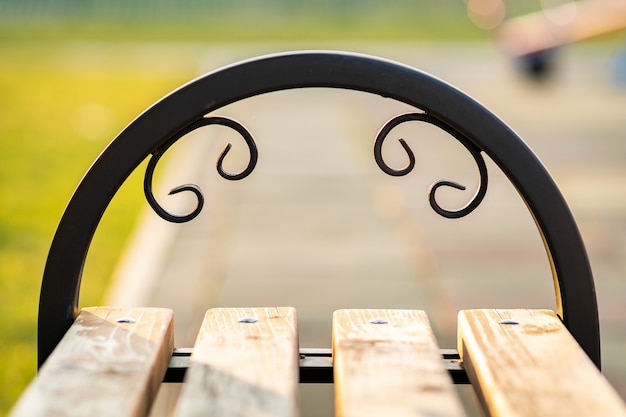 Closeup of wooden park bench with metal handgrip outdoors.