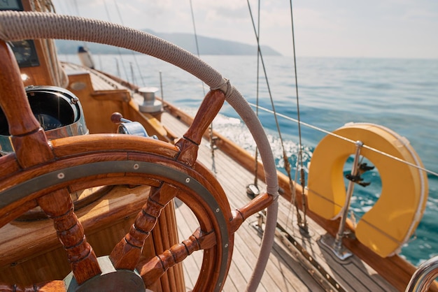 Closeup of wooden steering wheel on empty boat sailing the\
ocean closeup of empty boat deck with rigging cables wooden\
steering wheel sailing the ocean