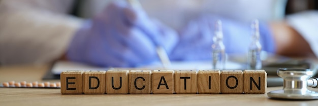Photo closeup of word education collected of wooden blocks in raw doctor in medical uniform writing