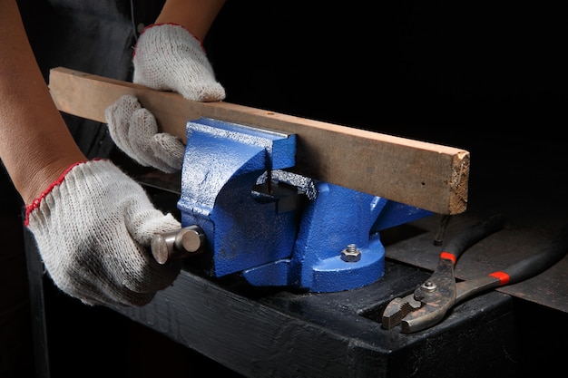 Closeup workers hands on a  wooden plank locked in the iron vise