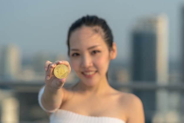 Closeup working woman in casual suit holding bitcoin over the cityscape blurred background, business